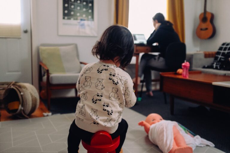 Una niña juega en el piso mientras una persona adulta trabaja en su escritorio