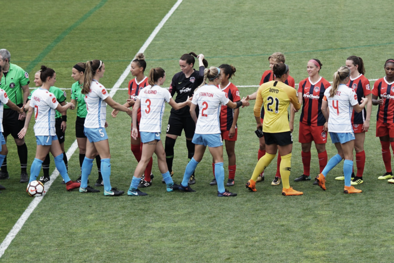 Jugadoras de dos equipos de fútbol se saludan en la cancha