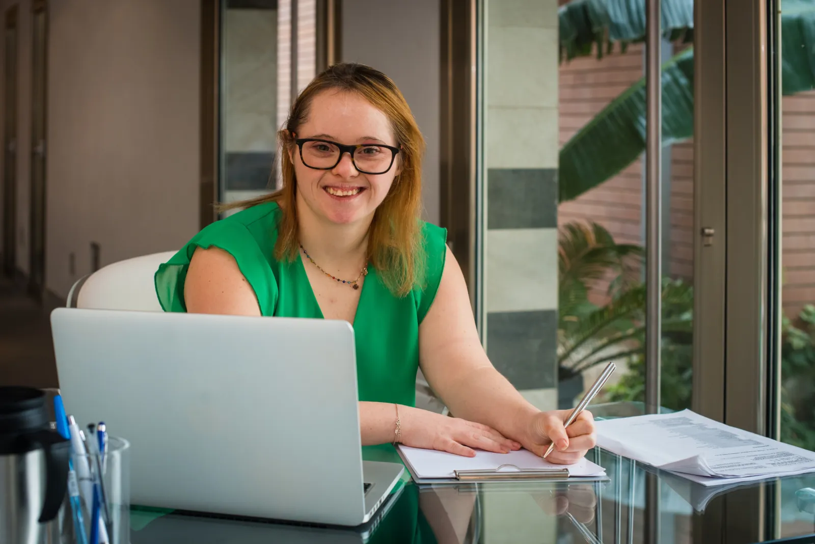 Mujer sonriente trabajando con su laptop mientras toma notas